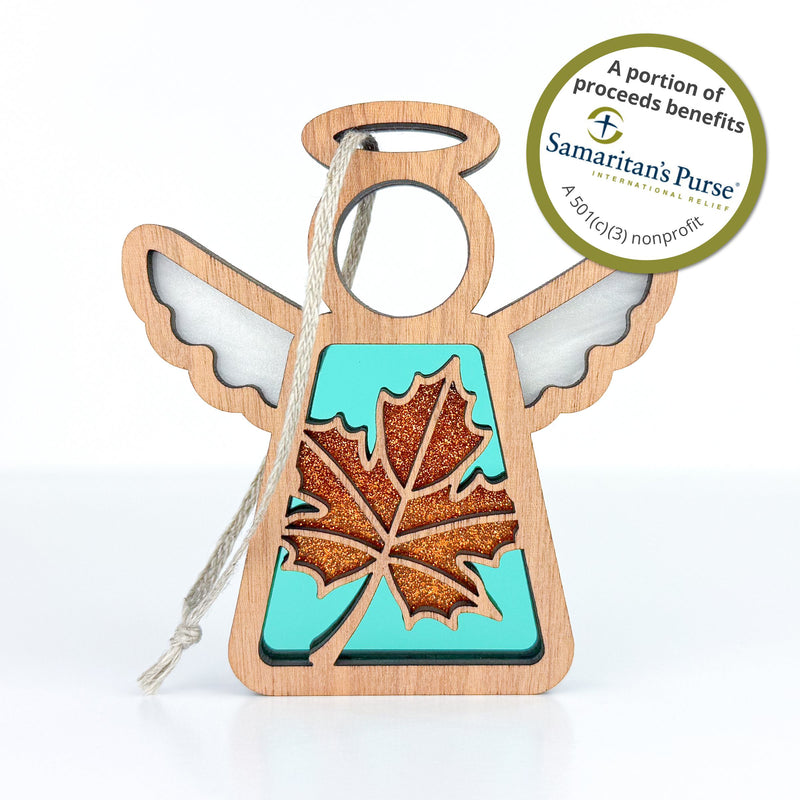 The Forged Flare® Sugar Maple Leaf for Charity Ornament is a 3.5"H Mother's Angels® wooden angel with a glittery orange maple leaf, teal background, twine loop, and a sticker supporting Samaritan’s Purse charity.