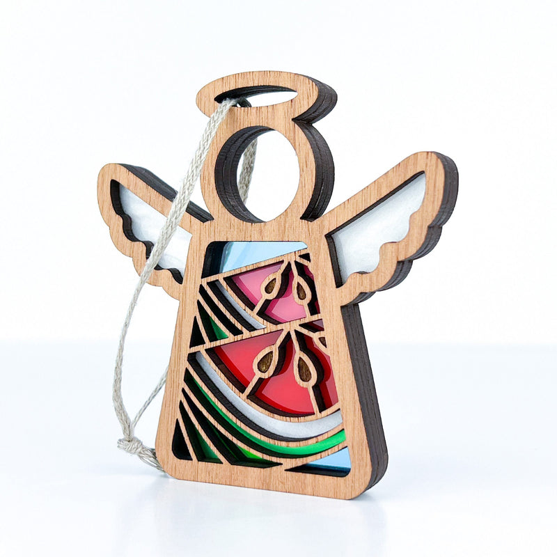 The Forged Flare® Summer Watermelon Ornament is a 3.5" Mother's Angels® wooden angel figurine with cut-out wings, a circular halo, and stained-glass effect details. Includes hanging string. Background is plain white.