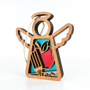 The Teacher Ornament by Forged Flare® is a 3.5" wooden angel figurine from the Mother's Angels® collection, featuring outspread wings and a halo. The ornament has a cutout design in the body that showcases a red apple and two yellow pencils on a blue background, with a hanging loop threaded through a hole at the top of the halo.