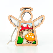 The Forged Flare® Mother's Angels® Toadstool Mushroom Ornament is a 3.5" wooden angel figurine with white wings, holding a red and yellow stained-glass style toadstool. Includes string for hanging as a Christmas tree ornament. Plain white background.