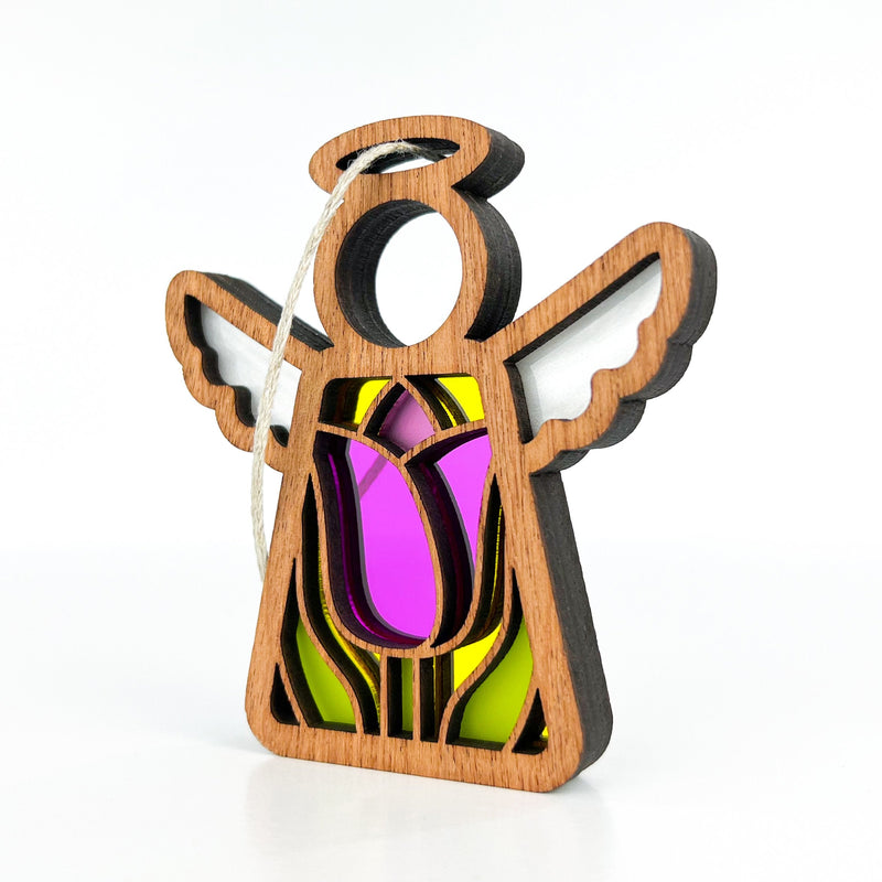 The Tulip Ornament, a 3.5" angel figurine from the Mother's Angels® collection by Forged Flare®, features a wooden design with cut-out sections filled with colorful stained glass. This angel has a striking purple and yellow pattern on its body, accompanied by white wings and a halo. Perfect as a Christmas tree ornament, it comes equipped with a string for easy hanging against any plain white background.