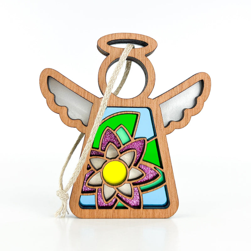 The Water Lily Ornament by Forged Flare® is a 3.5" wooden angel with cut-out wings, stained-glass-style details, and a bright water lily design, hanging by a cream string. Part of the Mother's Angels® collection.