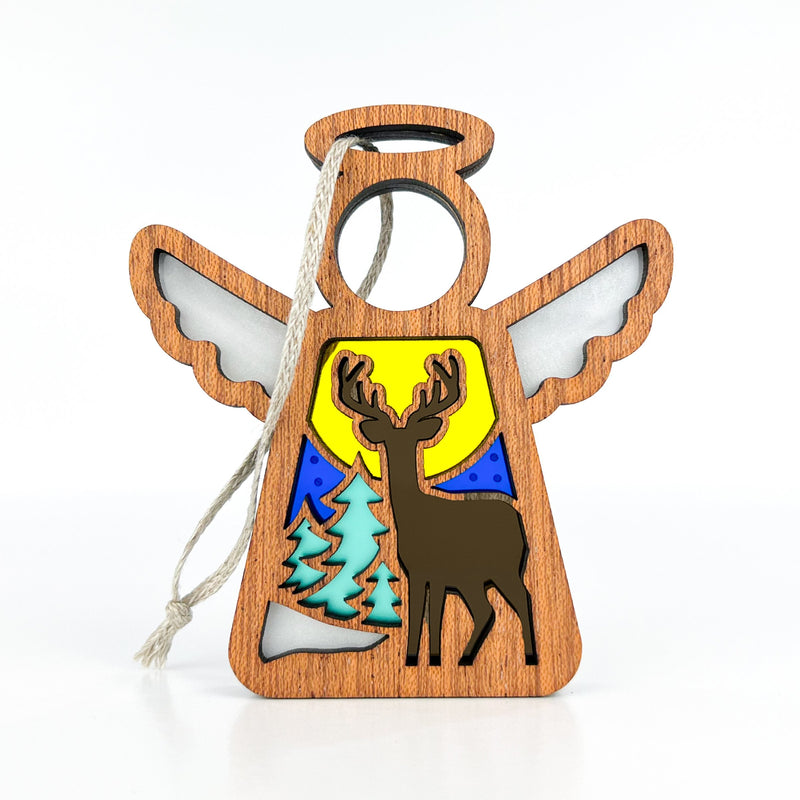 The Forged Flare® Winter Deer Ornament is a 3.5" wooden angel figurine from Mother's Angels®, featuring a deer with green trees and a yellow moon or sun—perfect for adding wintry charm to your seasonal decor.
