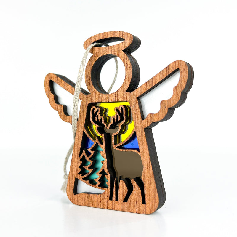 The Forged Flare® Winter Deer Ornament is a 3.5" Mother's Angels® figurine featuring an angel with cutout wings, a deer and tree silhouette, stained glass-style background, and hanger—ideal for winter decor.