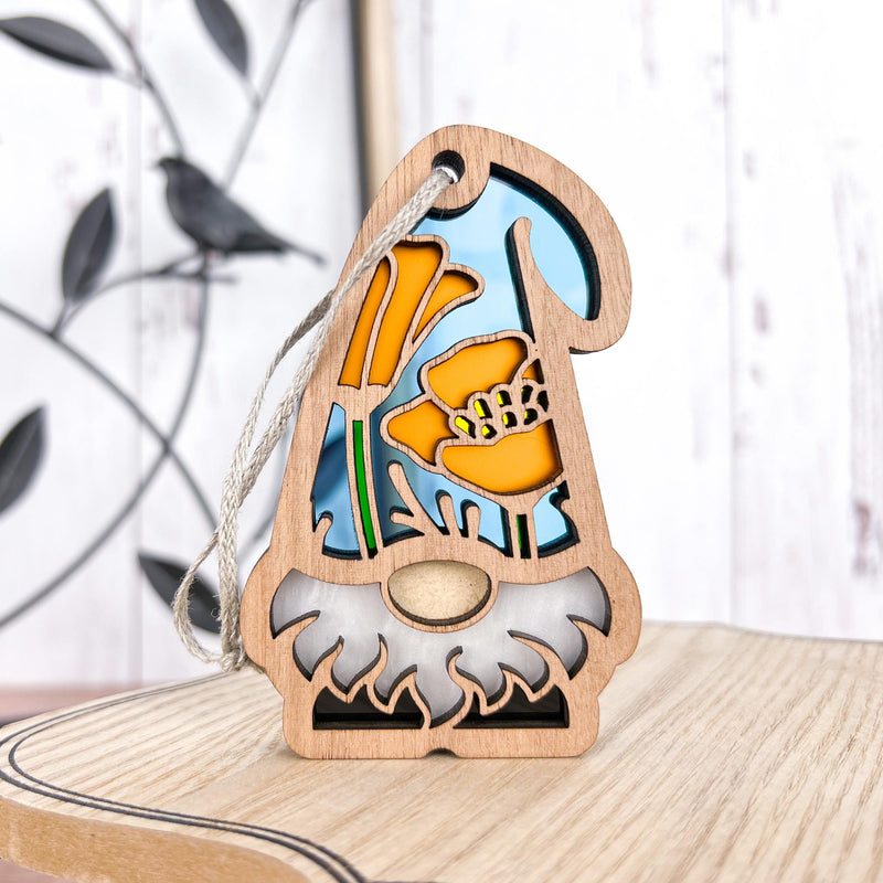 The Forged Flare® California Poppy Ornament, 3.75" tall from the Nature's Gnomes™ collection, features a bearded gnome with stained-glass-style poppies and a blue background, perfect for hanging in your home or garden.