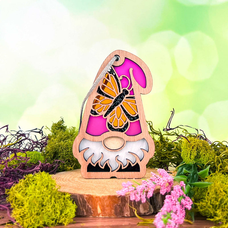 The Monarch Butterfly Ornament (3.75" H) from Nature’s Gnomes™ by Forged Flare® features a wooden gnome with a pink hat and painted butterfly on a tree slice, adorned with green moss and purple flowers—perfect for garden décor.