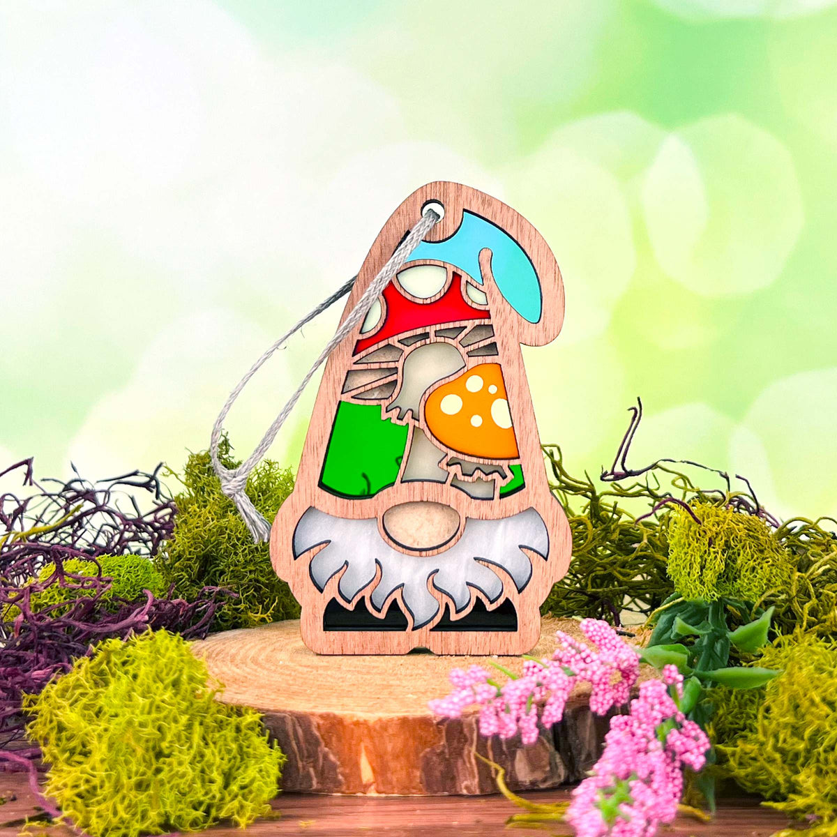 The Forged Flare® Toadstool Mushroom Ornament (3.75" H) by Nature's Gnomes™ features a colorful gnome with a red, white-spotted toadstool on a wood slice, with moss and pink flowers, perfect as a whimsical garden gift.