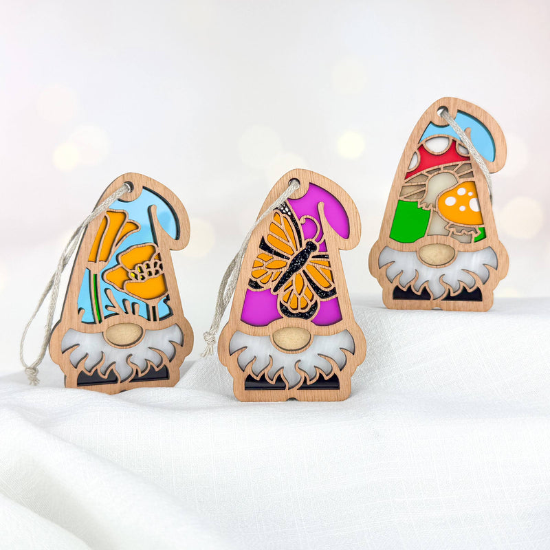 The Forged Flare® Nature's Gnomes™ 3-piece bundle features charming 3.75" wooden gnome ornaments with California Poppy, Monarch Butterfly, and Toadstool Mushroom designs—an ideal garden gnome gift, shown upright on a white fabric background.