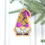 The Forged Flare® Monarch Butterfly Ornament, a 3.75" garden gnome with a purple hat and monarch butterfly, hangs from a pine branch—a delightful addition from the Nature’s Gnomes™ collection.