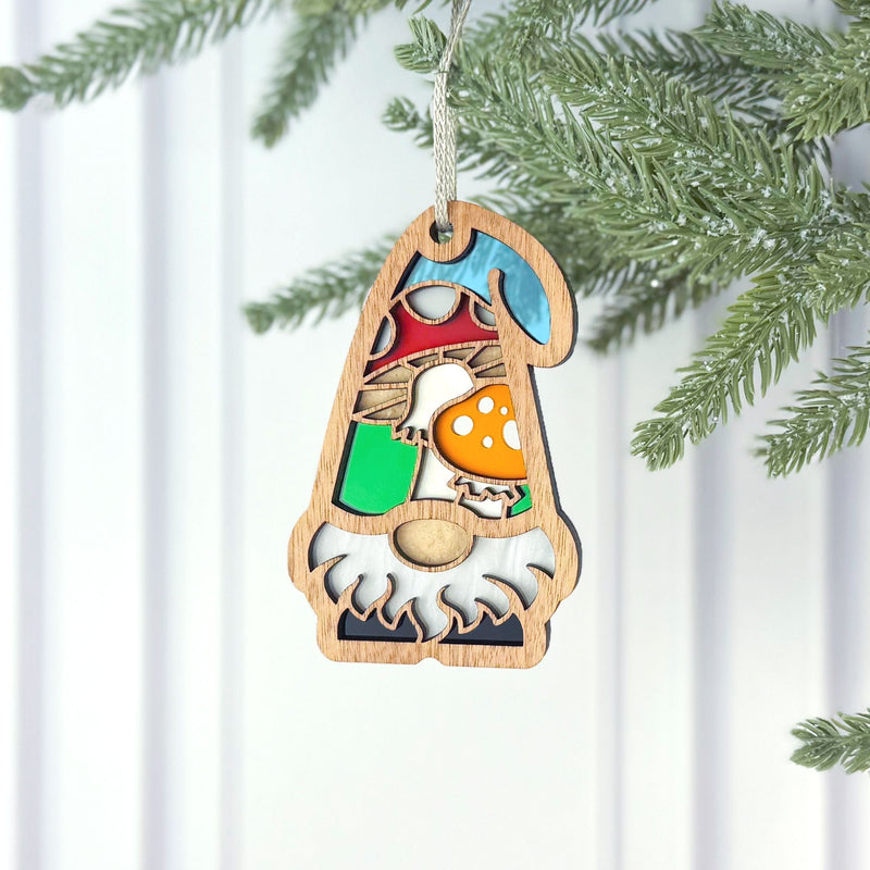 The Forged Flare® Toadstool Mushroom Ornament (3.75"H) by Nature's Gnomes™ features a garden gnome with a white beard and colorful hat, hanging from a pine branch against a white background.