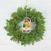 A green pine wreath hangs on a white brick wall, centered with Forged Flare®'s Toadstool Mushroom Ornament—a 3.75" garden gnome from the Nature's Gnomes™ collection holding a red toadstool mushroom.