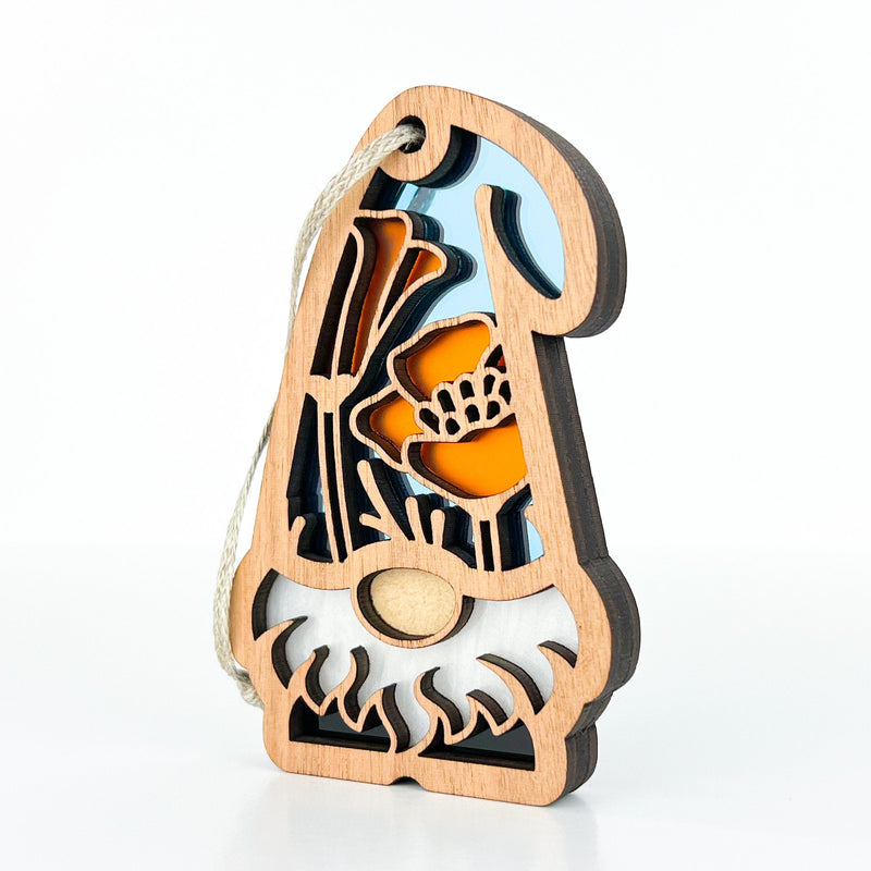 The California Poppy Ornament by Forged Flare® is a 3.75" wooden gnome from the Nature’s Gnomes™ collection, featuring a white beard, orange poppy cutouts with a blue background, and a rope loop for hanging.