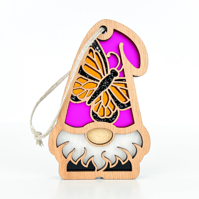 The Forged Flare® Monarch Butterfly Ornament from the Nature’s Gnomes™ collection is a 3.75" wooden garden gnome with a white beard, pink hat, orange butterfly cutout, and a white hanging string.