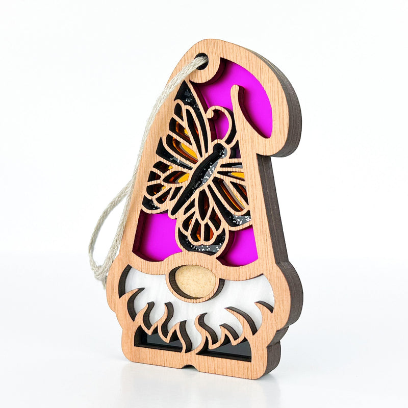 The Forged Flare® Monarch Butterfly Ornament is a 3.75" wooden garden gnome with a white beard, yellow nose, purple hat with butterfly cutout, and hanging loop, part of the Nature’s Gnomes™ collection.
