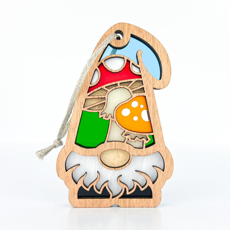 The Toadstool Mushroom Ornament by Forged Flare® is a 3.75" wooden garden gnome with a blue hat, white beard, and stained-glass-style toadstool mushrooms on its body, plus a string loop for hanging. Background is plain white.