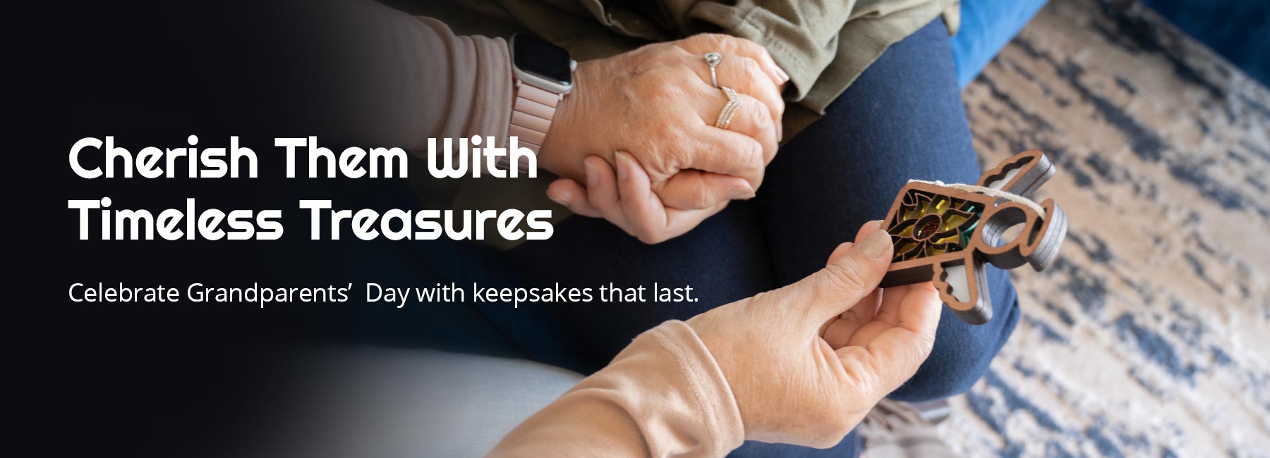 Cherish Them With Timeless Treasures. Celebrate Grandparents' Day with keepsakes that last. An intimate moment showing a grandchild gifting a Mother’s Angels® ornament to their grandparent. The image captures the sentiment and suggests thoughtful grandparents day gift ideas.