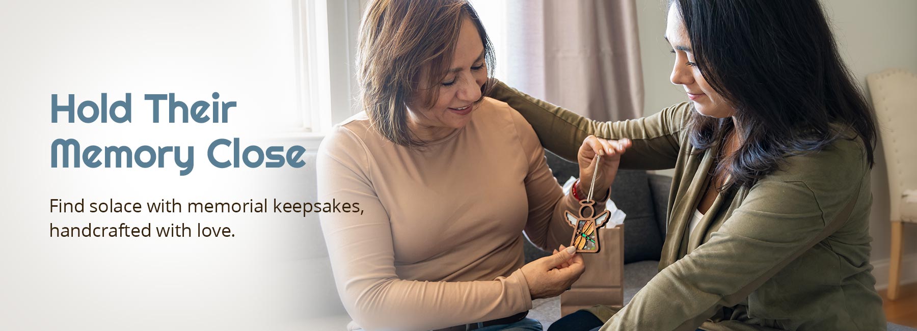 Hold Their Memory Close. Find solace with memorial keepsakes, handcrafted with love. Two women share a moment, giving a Forged Flare® Mother’s Angels® ornament as a memorial gift, embodying sympathy and bereavement, suitable for celebration of life decorations.