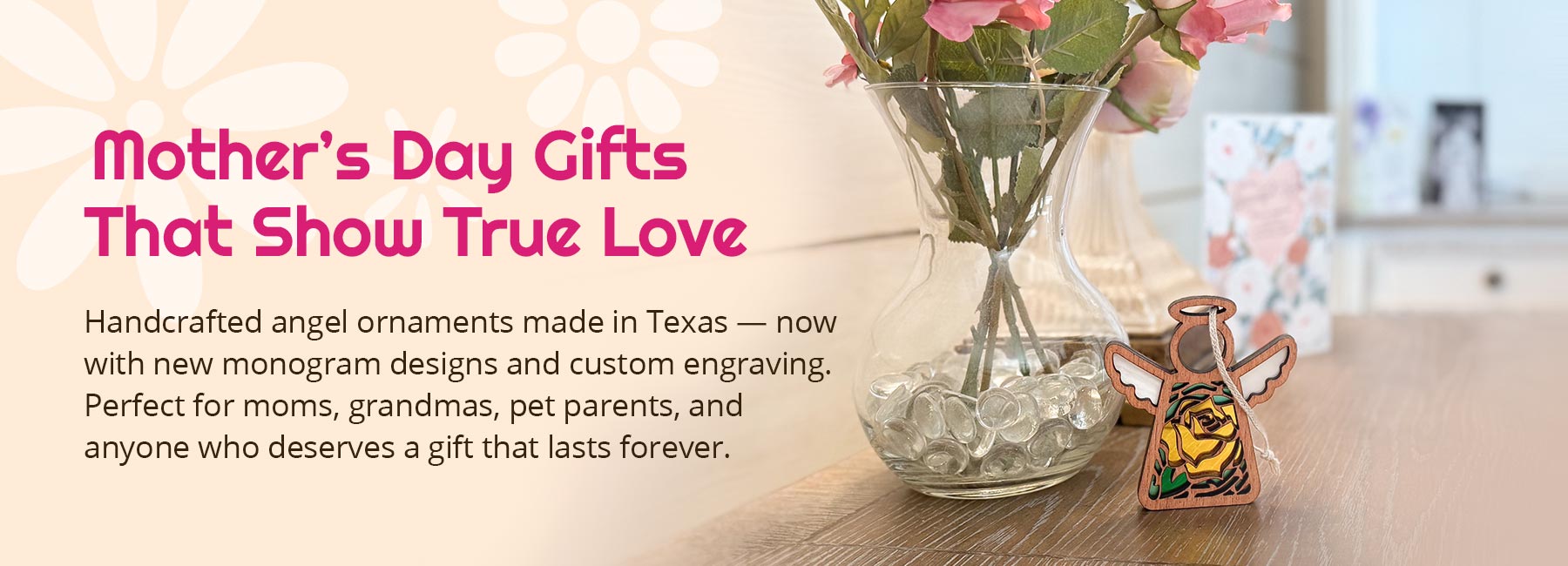 Yellow rose Mother’s Angels® ornament displayed next to a vase of pink flowers. There's a blurred desk with a greeting card in the background and a wedding photo of parents. Text reads: Mother's Day Gifts That Show True Love. Handcrafted angel ornaments made in Texas — now with new monogram designs and custom engraving. Perfect for moms, grandmas, pet parents, and anyone who deserves a gift that lasts forever.