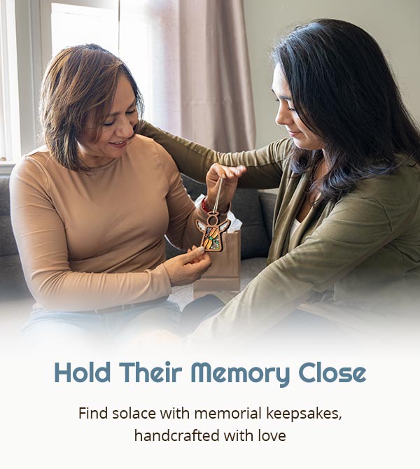 Hold Their Memory Close. Find solace with memorial keepsakes, handcrafted with love. Two women share a moment, giving a Forged Flare® Mother’s Angels® ornament as a memorial gift, embodying sympathy and bereavement, suitable for celebration of life decorations.