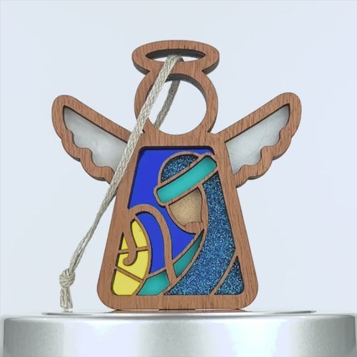 A wooden angel nativity ornament featuring a stained-glass style image of a serene figure draped in blue, clutching a yellow object. The angel has wings, a halo, and is adorned with a hanging string. With vibrant blue and yellow accents, this piece perfectly complements your nativity set.