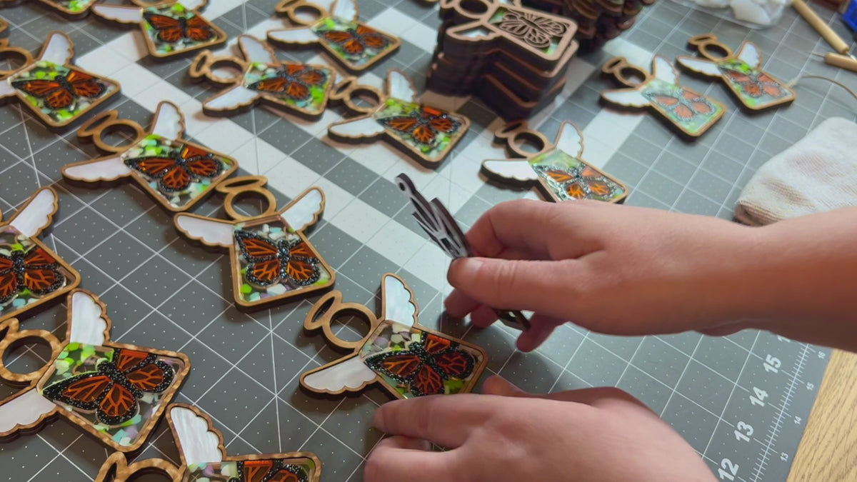 Video demonstration of how we make our handcrafted ornaments. The image consists of  a small batch of monarch butterfly Mother’s Angels® ornaments. Text reads: Handcrafted by a small business in Texas! A peek at how we make our ornaments. 