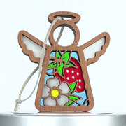A wooden Christmas ornament shaped like an angel with a halo and outstretched wings. This delightful strawberry ornament features a colorful design including a red strawberry, green leaves, and a white flower on its body. It hangs gracefully by a braided linen string.