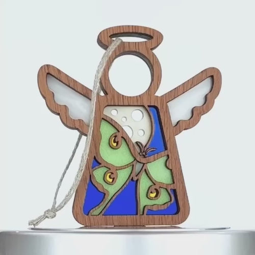 A wooden angel ornament with a cut-out design of a luna moth, showcasing large eyespots on its wings. The angel features a blue background, white wings, and a wooden halo, with a white string attached at the top for hanging.