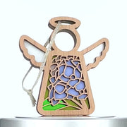 A wooden angel ornament featuring stained glass–style decorations on its body. The design includes intricate blue and purple floral patterns with green leaves, reminiscent of a hydrangea ornament. A string is attached to the top for hanging.