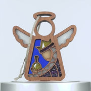 A wooden ornament shaped like an angel with wings, featuring a a purple wise man stained glass–style design. The angel holds a gold and green object, has a gold glitter crown, and a blue, purple, silver, and white color scheme. A braided linen string is attached for hanging.