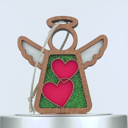 Wooden angel hearts ornament with white wings, a round halo, and two pink hearts in the center. The hearts are set on a green glittery background, and a braided linen string is attached for hanging. The ornament has a simple, yet charming design.