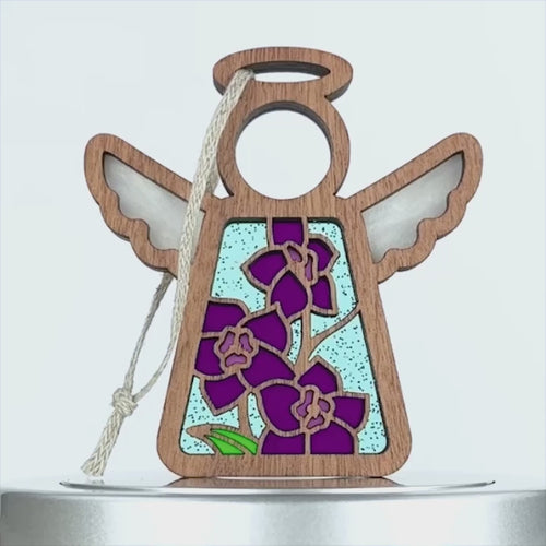 A decorative wooden angel with wings and a halo features a hollow circular head and a body filled with purple larkspur flowers set against a light blue background. A braided linen string is attached at the top for hanging, creating a charming larkspur ornament perfect for any space.