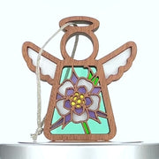 A wooden angel ornament adorned with a stained-glass-style columbine flower design in pastel shades of blue, purple, and yellow on its body. It has a halo and wings, with a string attached for hanging. The background is plain white.