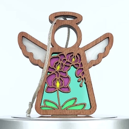A wooden angel ornament with cutout wings and halo, featuring a multicolored flower design. Purple orchid petals and yellow centers stand out against a blue and teal backdrop. A braided linen string is attached for hanging.