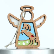 A wooden angel-shaped horse ornament with wing cutouts, a halo, and a rope loop for hanging. It features a horse rearing up on its hind legs, with a small red heart on its chest, set against a background of grass, flowers, and a blue sky.