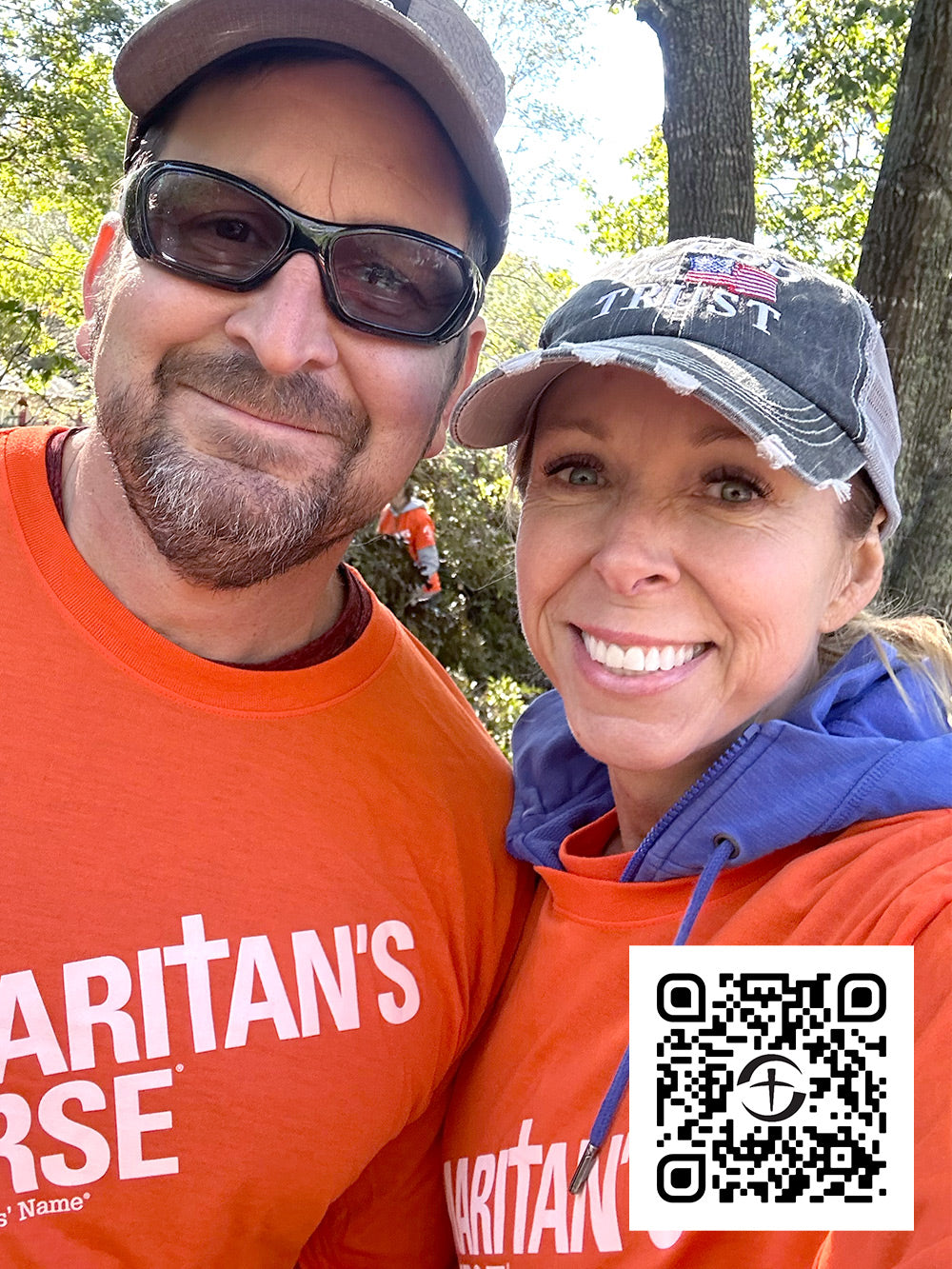 A man and a woman wearing orange "Samaritan's Purse" shirts and sunglasses smile at the camera. They stand outdoors with trees in the background. A QR code is visible in the bottom right corner.