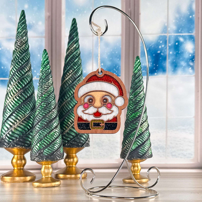 Santa Sweet Cheeks Christmas ornament with rosy cheeks hanging on a silver stand by a snowy window, a jolly Santa gift