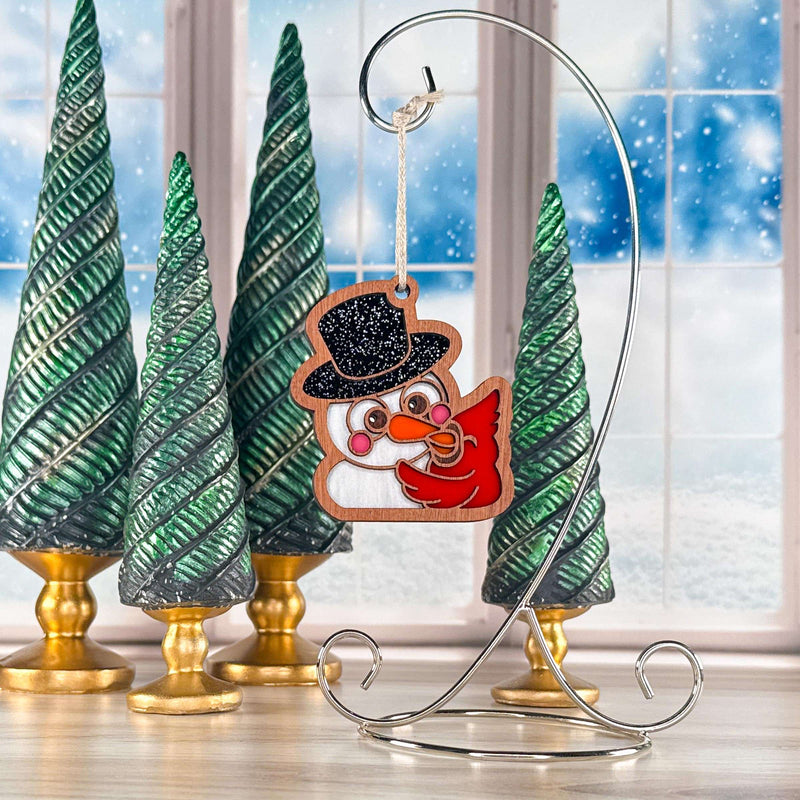Snowy Snuggles snowman and red cardinal Christmas ornament hanging on a silver stand by a snowy window