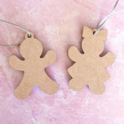 Two blank wooden Sweet Gingerbread Cookies Ornaments—a boy and a girl, each 3.5" tall—by Forged Flare® lie on a pink marbled surface. Each ornament comes with a string loop, perfect for hanging as festive holiday decor.