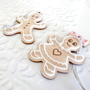 Forged Flare® Sweet Gingerbread Cookies Ornaments: Boy & Girl Set (3.5"H) features wooden ornaments with white icing-like designs, a pink bow, and string for hanging—perfect for holiday decor.