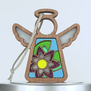 A wooden angel ornament with intricate cutouts and stained glass–style elements. The angel, adorned with a circular halo and outspread wings, features a colorful water lily floral design in the center. A braided linen string is attached for hanging.