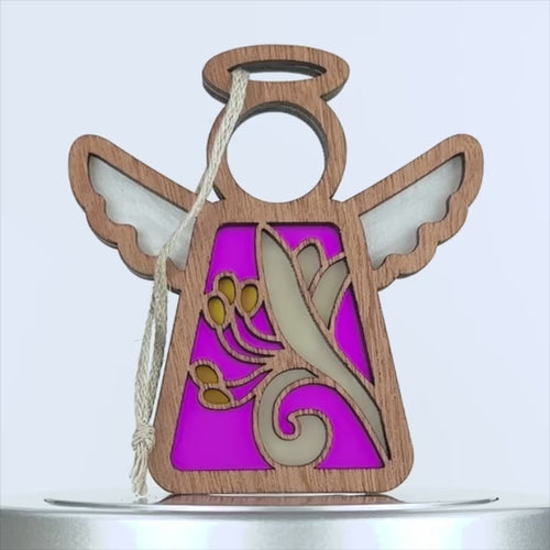 A wooden angel honeysuckle ornament with a string for hanging. The angel boasts intricate cut-out designs, including a floral pattern, and features a vibrant pink background. The ornament has wings and a halo, with the outer edge in a natural wood finish.
