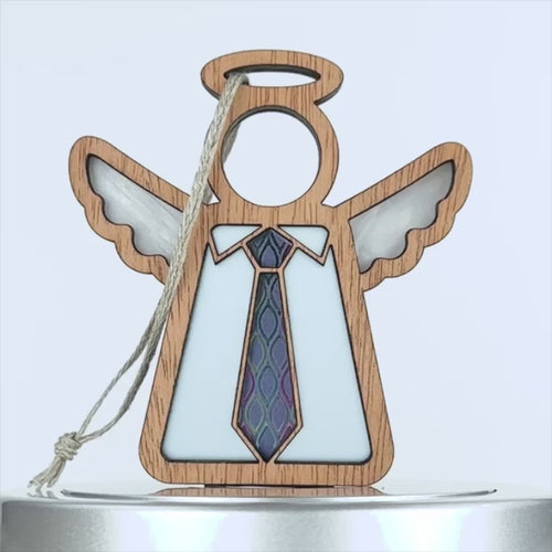 A wooden angel ornament with a hollow circle as a head, white wings, and a light blue body. The angel wears a colorful tie with a geometric pattern, making it an ideal Father's Day gift. A string is attached to the top for hanging.