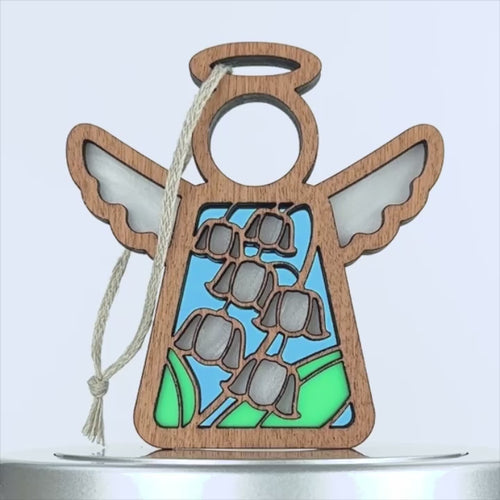 A wooden angel ornament with intricate cutouts, featuring a design of white lily of the valley flowers and green leaves on a blue background. The angel has a simple halo and wings, and a string is attached for hanging. The overall style is delicate and decorative.