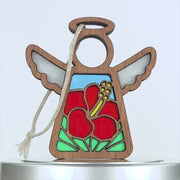 A wooden ornament shaped like an angel, featuring vibrant stained glass-like designs. The angel has red hibiscus flower patterns on its dress, white wings, and a halo. A string is attached for hanging. The design elements include intricate woodwork and colorful detailing.