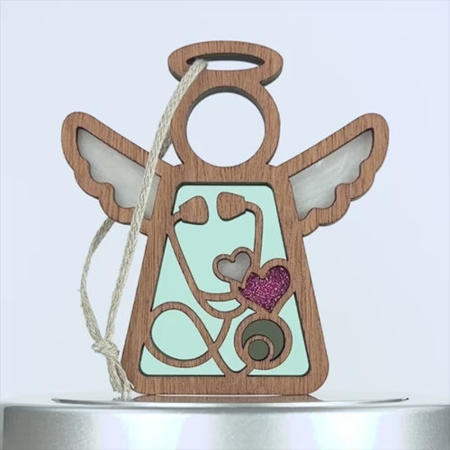 A wooden angel-shaped ornament with white wings and a halo at the top.Perfect as a thoughtful gift for a nurse, it comes with an attached braided linen string for hanging.