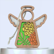 A marigold ornament crafted from wood features cut-out wings and a halo. The body showcases vibrant stained glass-style sections displaying yellow and orange flowers with green leaves. A braided linen string is attached for hanging against a plain white background.