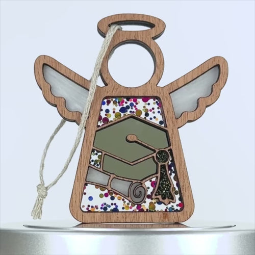 A wooden graduation ornament featuring a stained glass middle section with images of a graduation cap, diploma, and a gold key. The stained glass–style background is adorned with colorful speckles, and a braided linen string is attached for hanging.