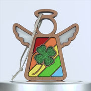 A wooden angel ornament with white wings, a halo, and a colorful stained glass–style body featuring a green glittery four leaf clover in the center. A braided linen string hangs from the top left for easy display. The background is plain white.