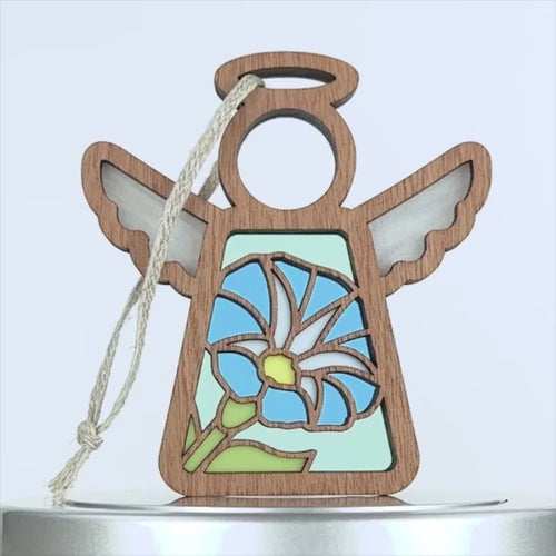 Wooden angel ornament with a stained glass-inspired design featuring a blue and white morning glory flower. The ornament includes a braided linen string affixed to the top. The background is white.