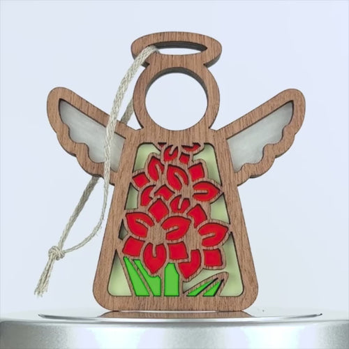 Wooden angel ornament with cutouts, featuring red flowers and green leaves in a stained glass style. The gladiolus ornament has a braided linen string for hanging, making it suitable for holiday decorations or gifts. The background is white.